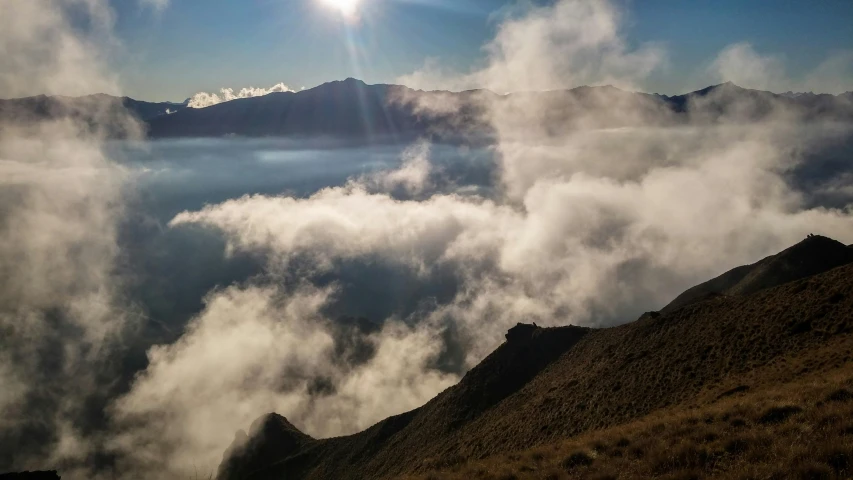 sun peeks above clouds over an arid mountain landscape