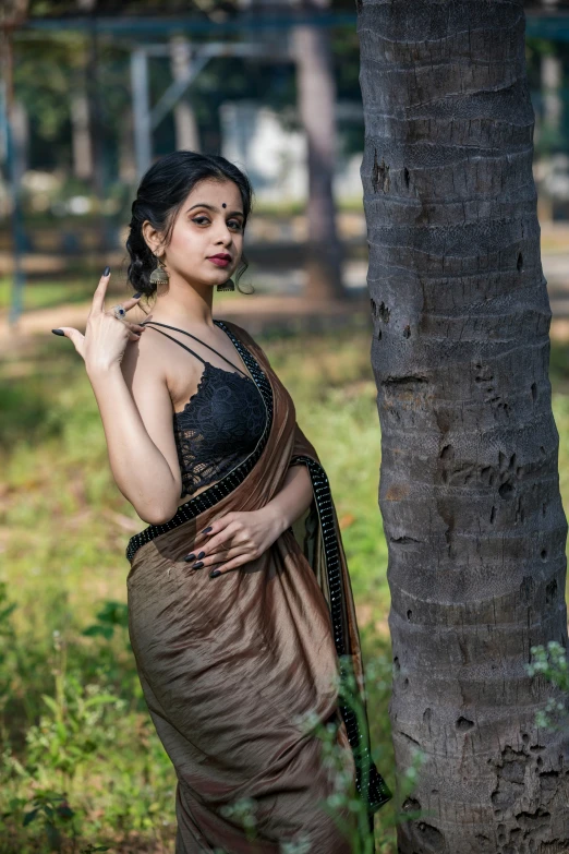 a woman posing in front of a tree, with her finger on her lip