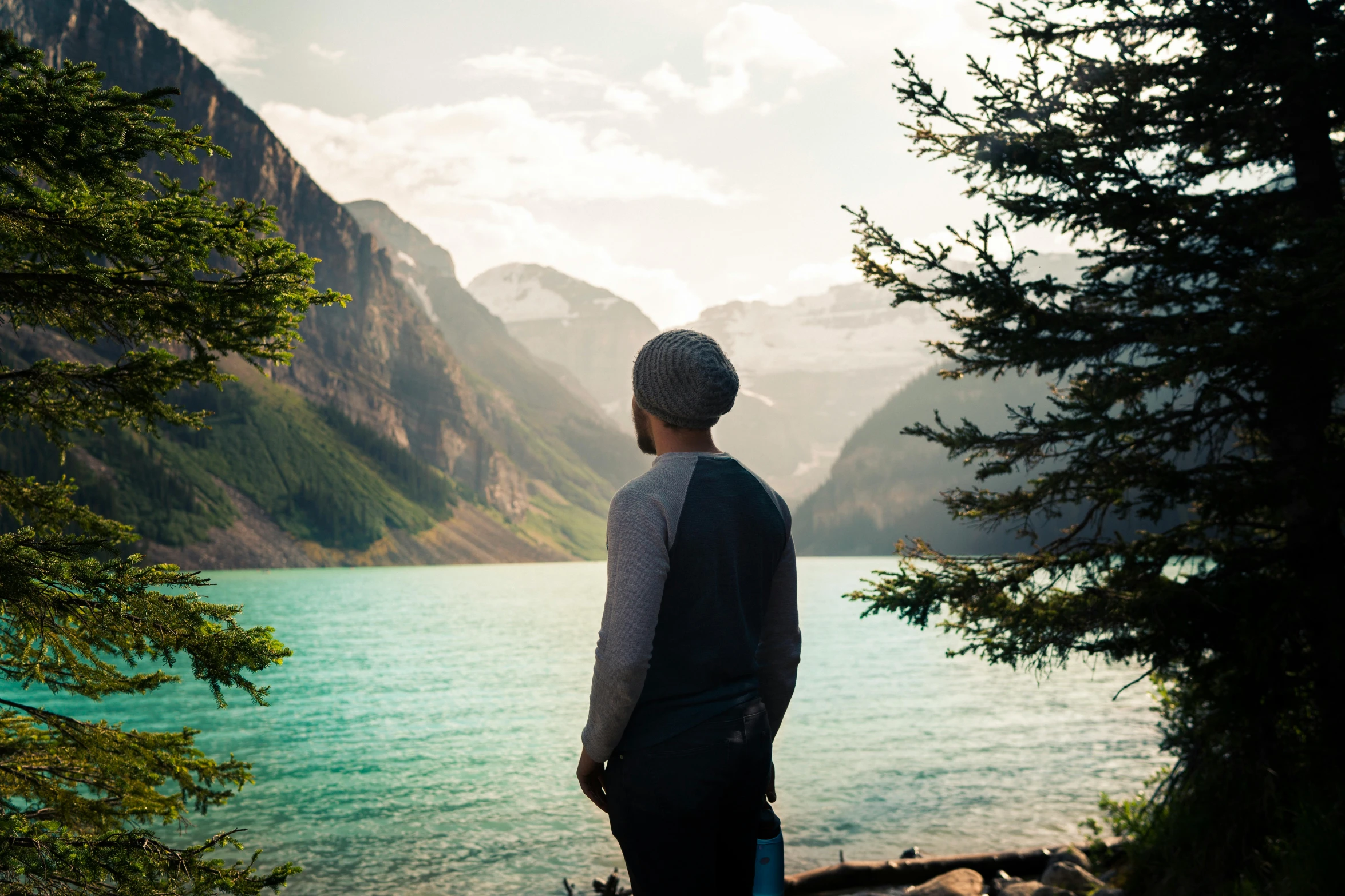 the back end of a man looking out on a lake with a mountain range in the distance