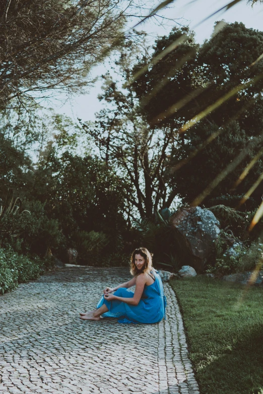 a woman sitting on a cobblestone path by the woods