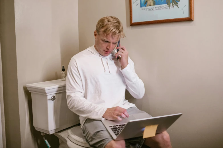 a young man sitting on top of a toilet talking on the phone