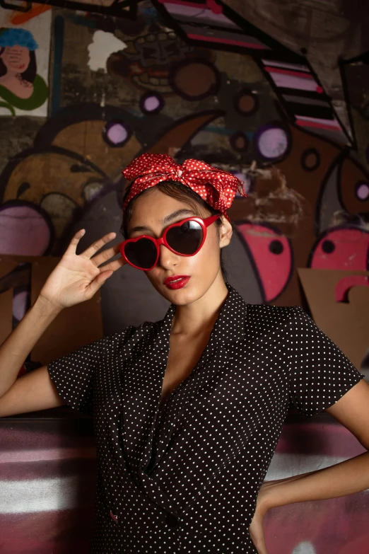 a woman wearing a polka dot dress poses with sunglasses on her head