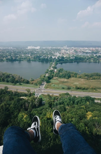 someone in jeans, shoes and sneakers is looking down on the river from a high rise