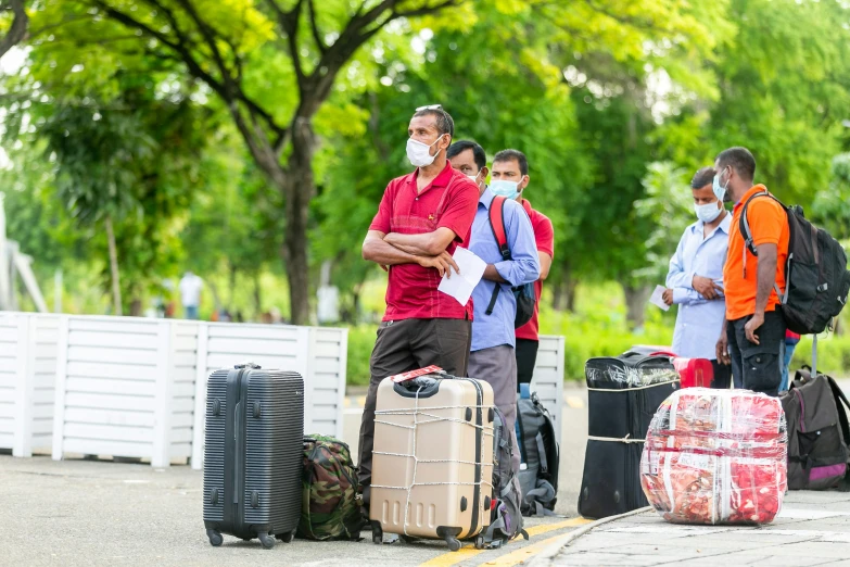 two men and one woman wearing face masks stand behind their luggage