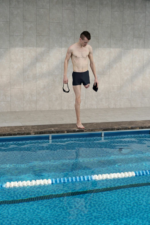 a guy is standing near the edge of the pool holding an object