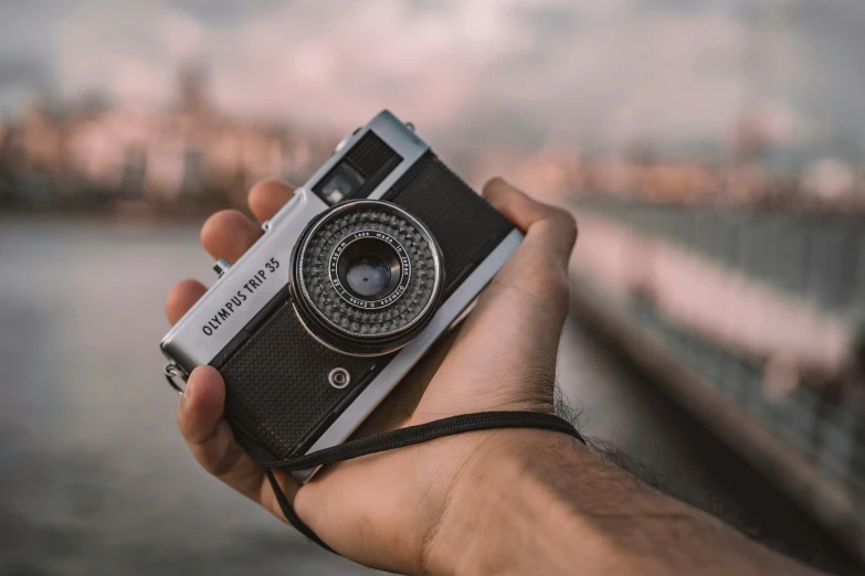 a hand holding a small camera in front of a body of water