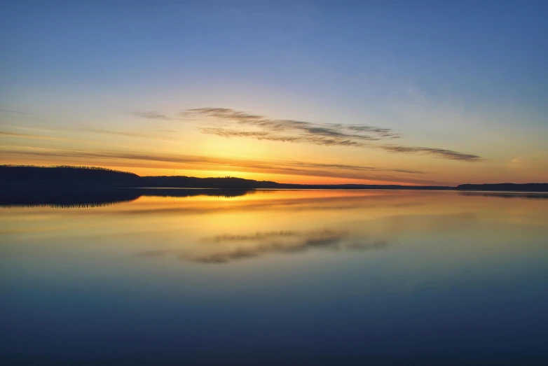 the sunset lights up the sky over a still body of water