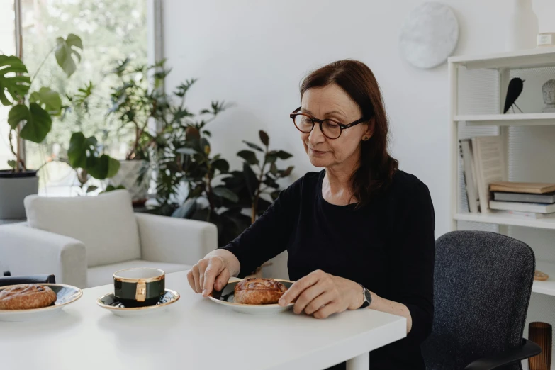 an older woman sits at a table and eats coffee and croissants