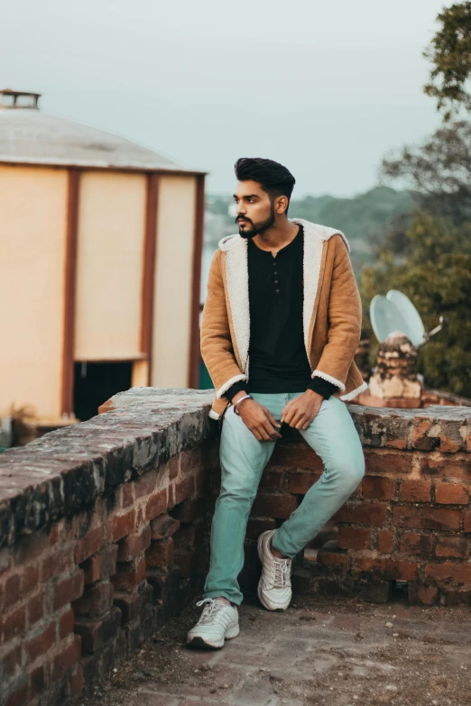 a man with a beard and black shirt sitting on a brick wall