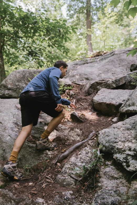 a man climbing on rocks while walking in the woods