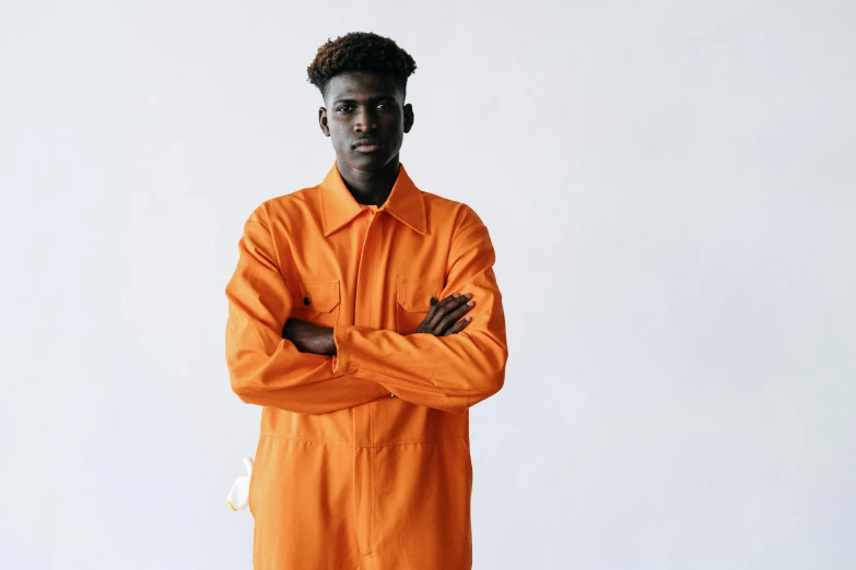 an african man wearing an orange jumpsuit stands in front of a white background