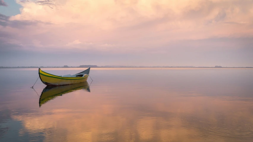 small boat floating in calm water against a sunset sky