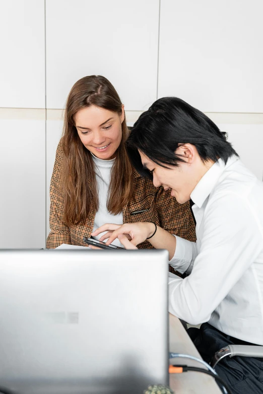 two people look at a laptop screen while sitting on the ground