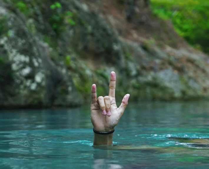someone making a peace sign out of their hand in a body of water