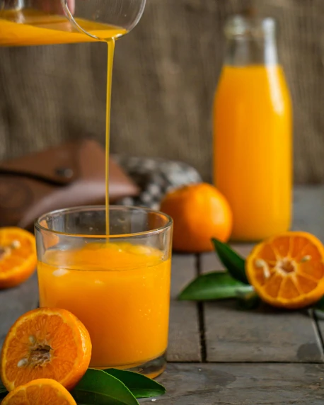 someone pouring orange juice into glass next to sliced clementine