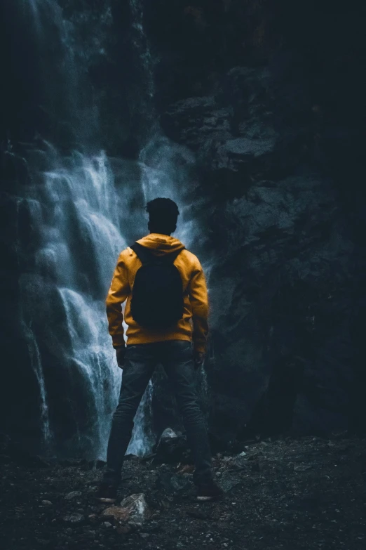 man standing by large waterfall in yellow jacket at night