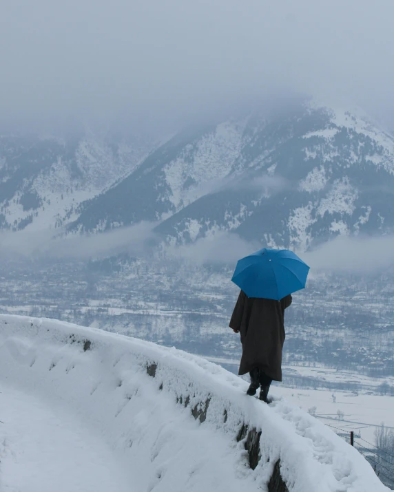 a person is standing on top of a snowy hill, with a blue umbrella