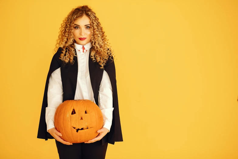 a girl in a halloween costume holding an orange pumpkin