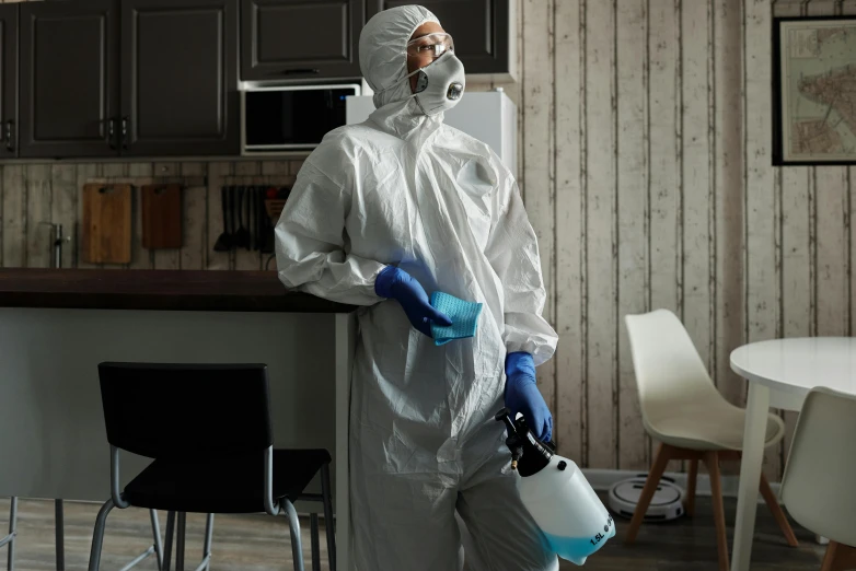 a man in white protective gear using a paint can to clean a kitchen