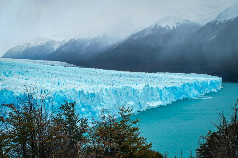 large glacier at edge of lake with mountains in background