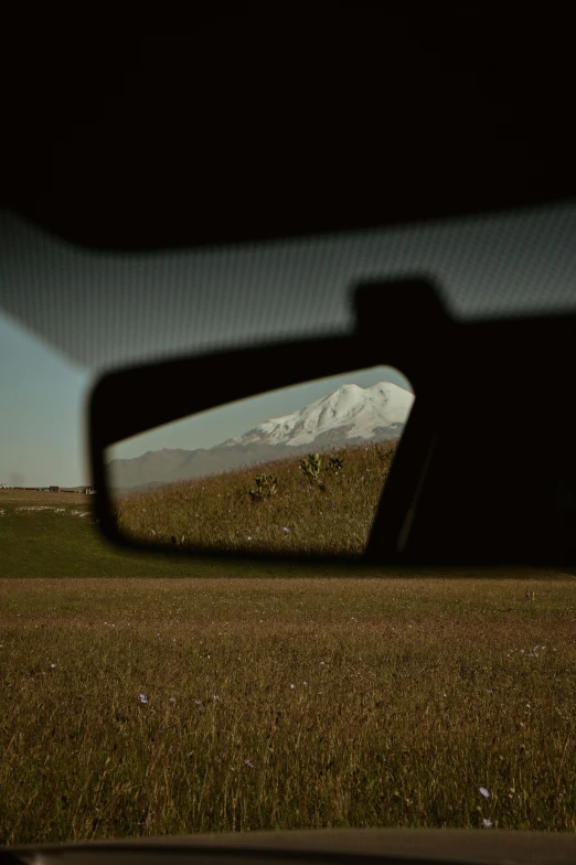 view of a snow covered mountain in the rear view mirror of a vehicle