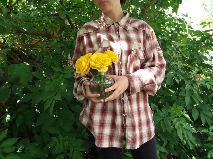 a woman is standing next to bushes holding a vase with flowers