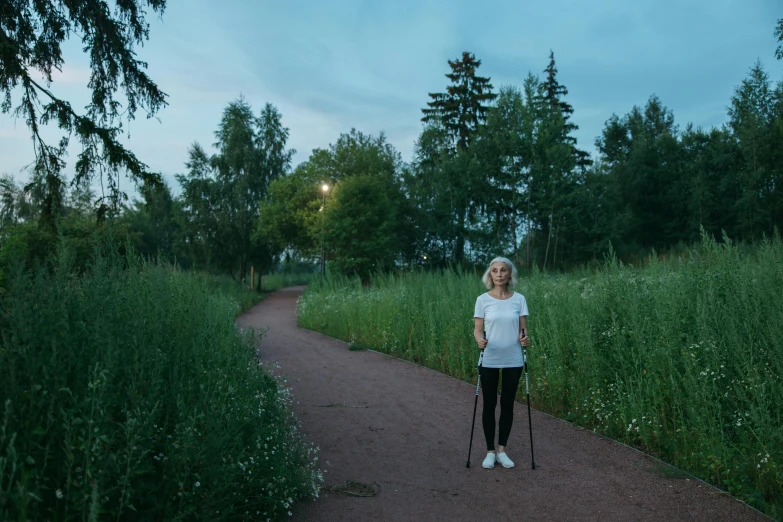 a woman walks with a cane along the trail in the tall grass