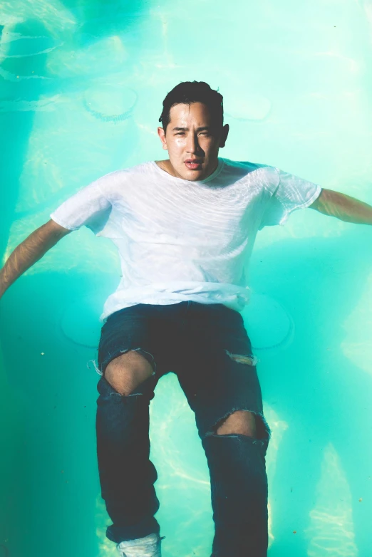 young man is standing in the water with ripped jeans on