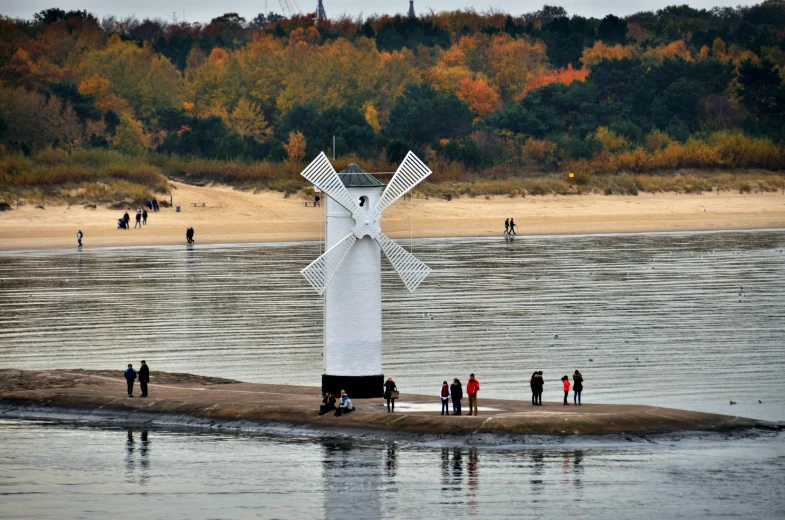 several people stand near a body of water with a large, white sculpture behind it