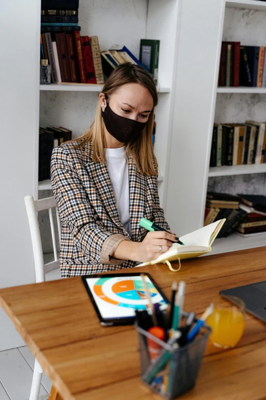 a woman sitting at a desk while wearing a black mask