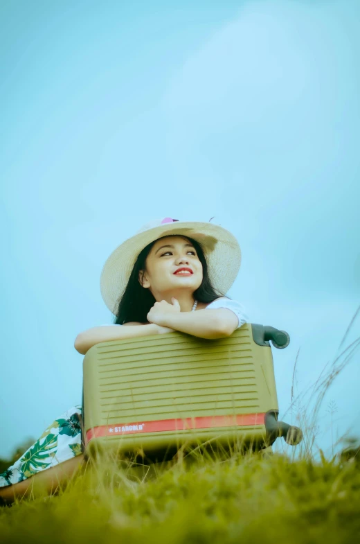 girl wearing hat leaning on luggage in field