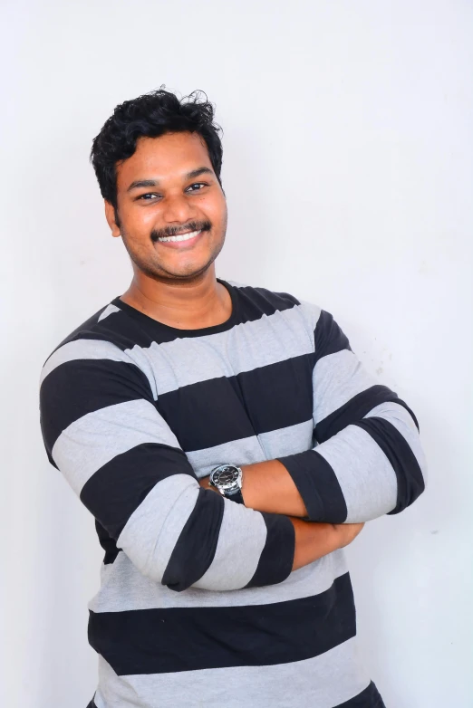 a smiling man in a black and white  shirt with his arms crossed