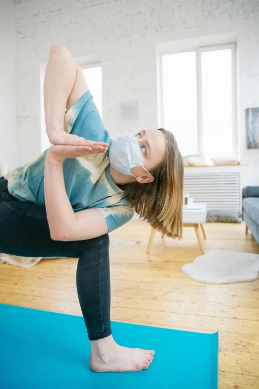 woman standing on one leg in a yoga position with one leg bent down and hands up to the head