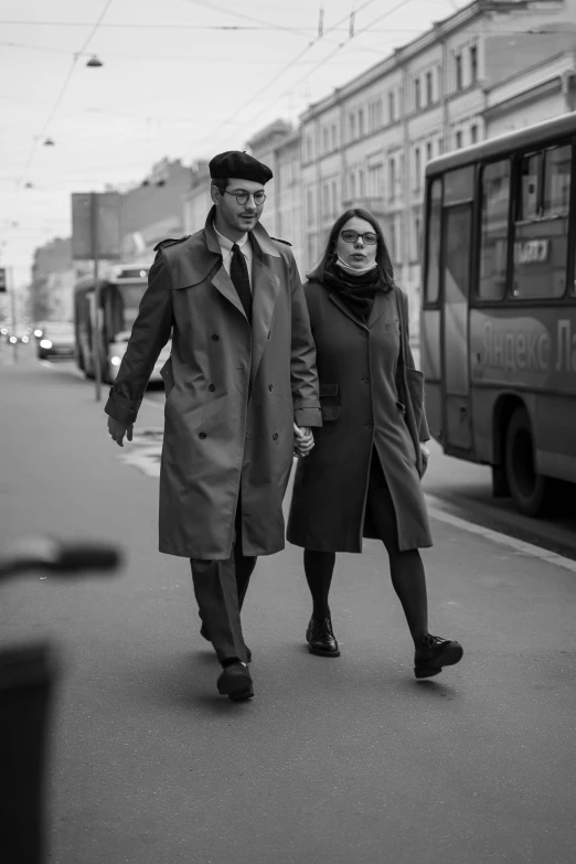 a black and white po shows a man in a coat, tie and black pants walking with a woman on the sidewalk