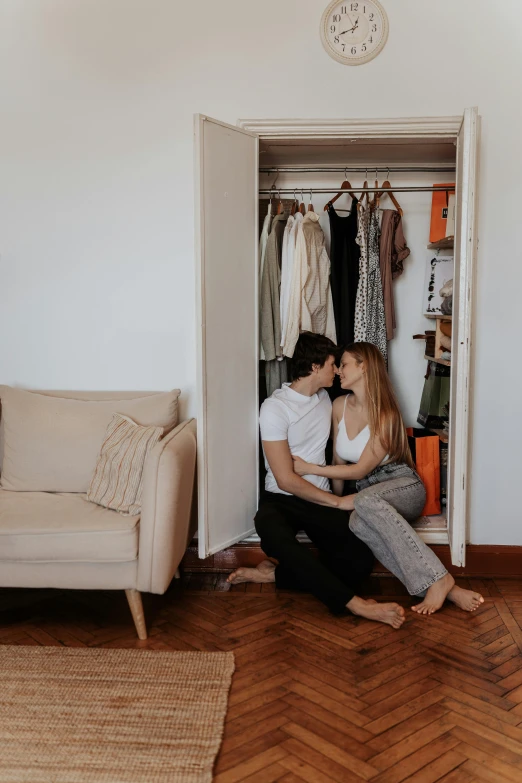 two people are sitting inside a closet with clothes hanging