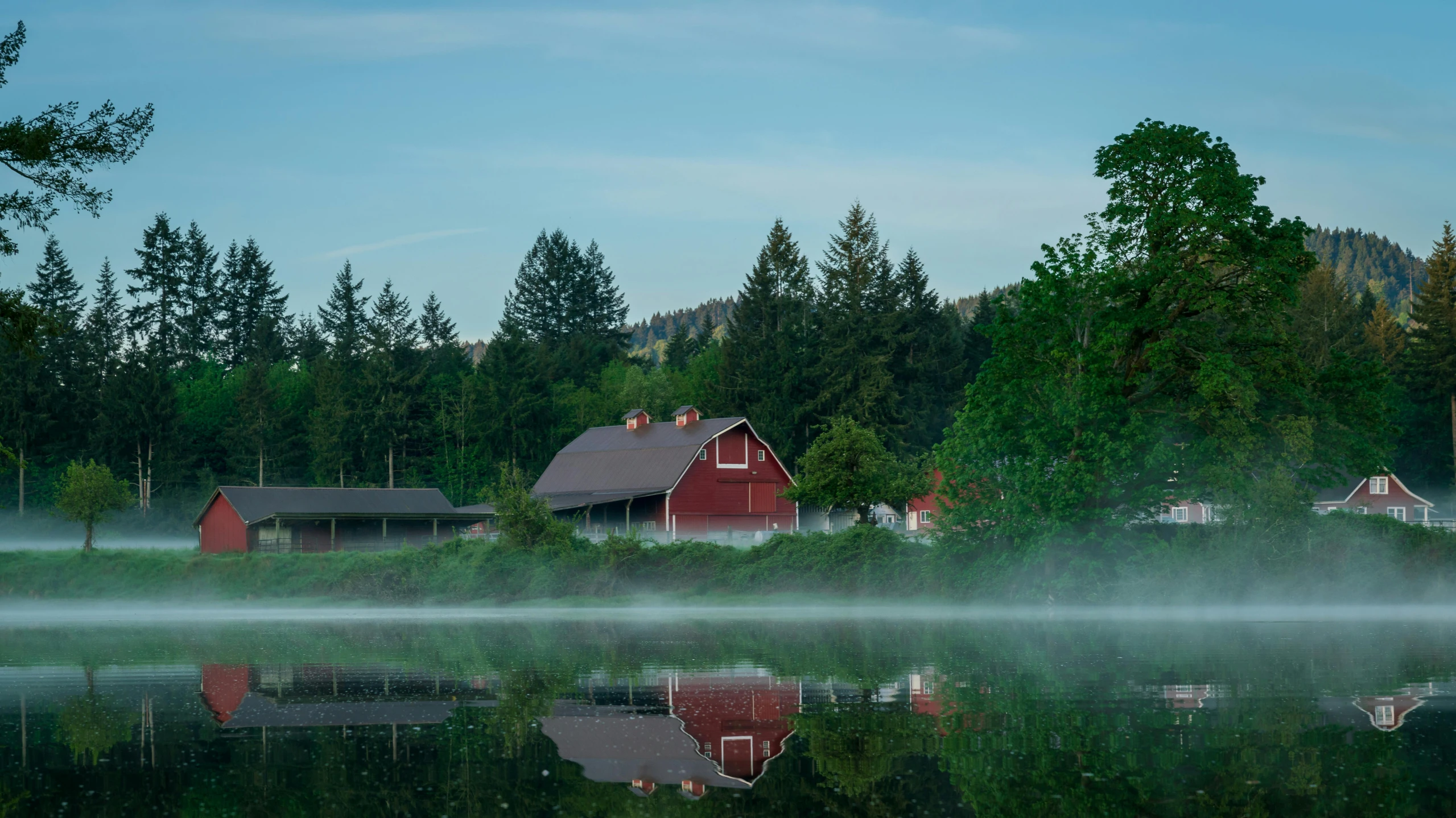 misty lake with a house on it and houses in the distance