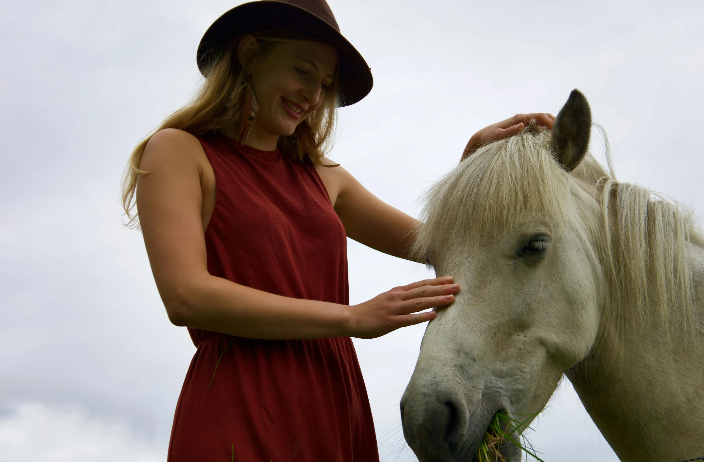 the woman is petting the horse with a hat on