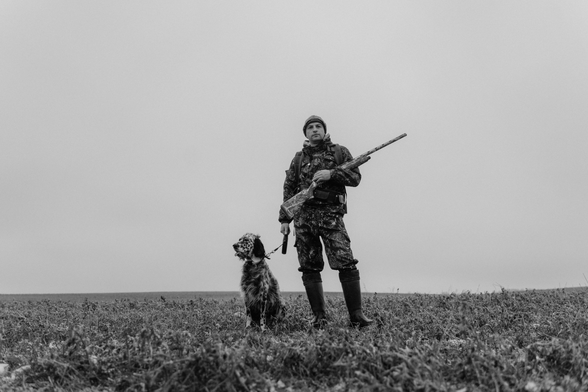 a person holding a rifle in the grass with a dog