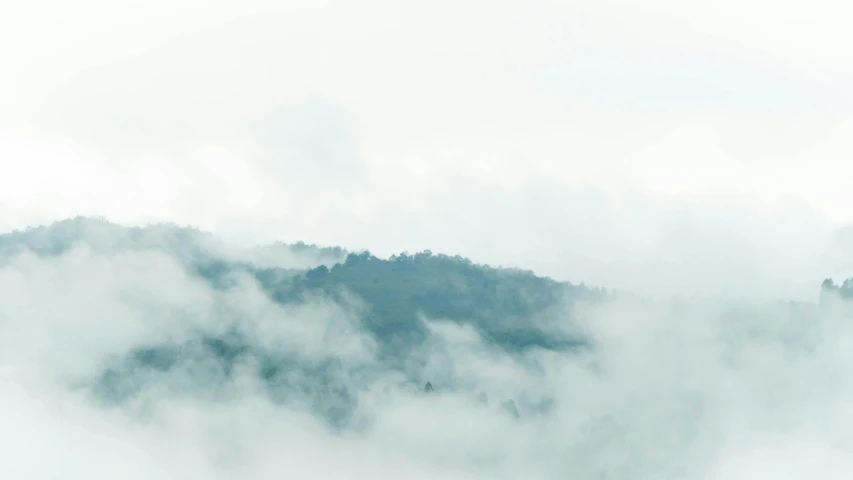 a green hillside with thick clouds hovering over it