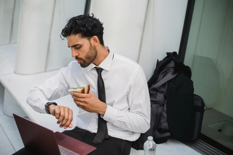 a man sitting down using a laptop and eating soing