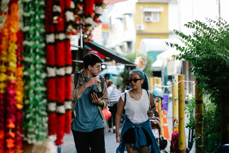 two people walking down a sidewalk in front of some colorful flowers