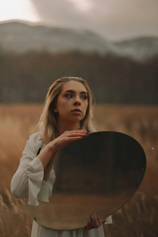 a girl with long hair holding a round mirror in front of her face