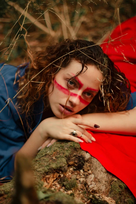 a woman in red and black painted face posing on a rock