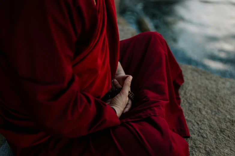 a man in red outfit sitting on the ground next to a river