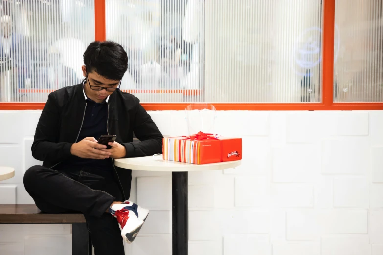 an asian man sitting down on a bench and looking at his phone