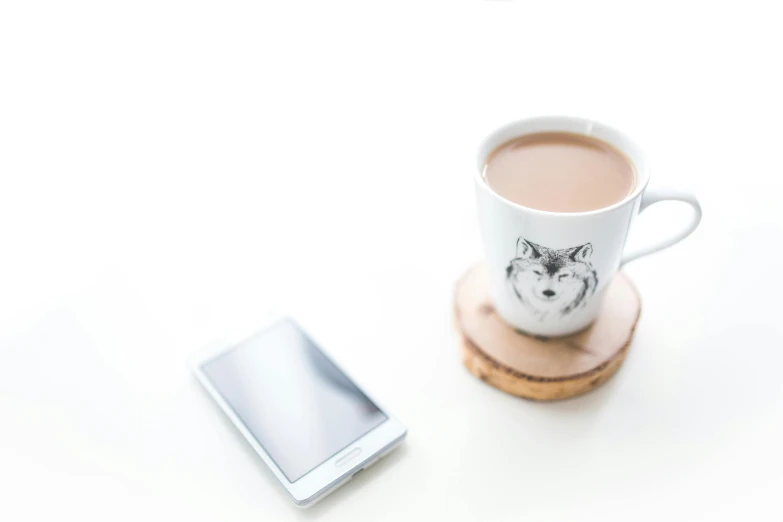 a white and black cat sticker on a cup next to a smart phone