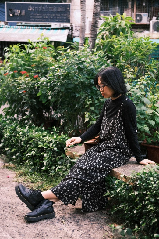 a woman sits on a wooden bench by some plants