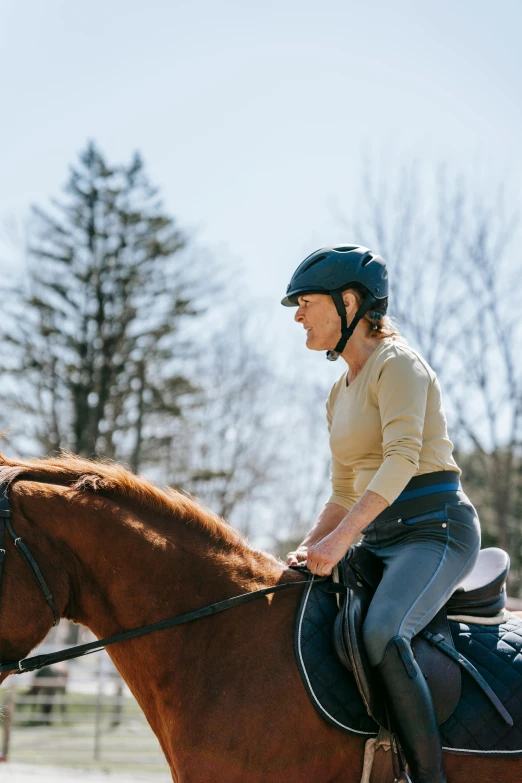 a woman rides a brown horse outside with trees