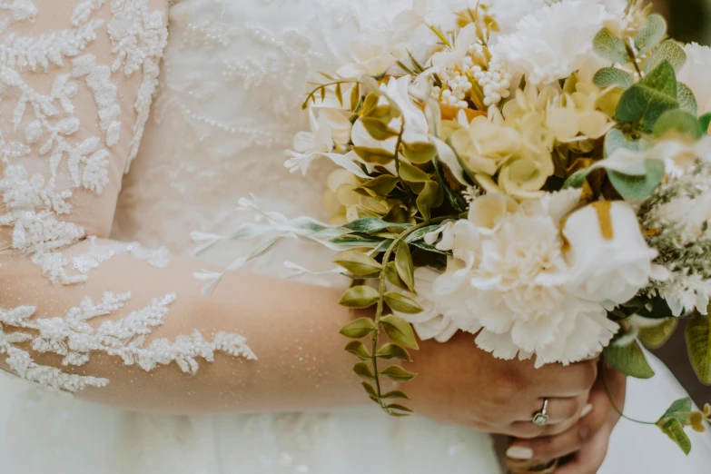 a bride holding bouquets of flowers, dressed in a lacy dress