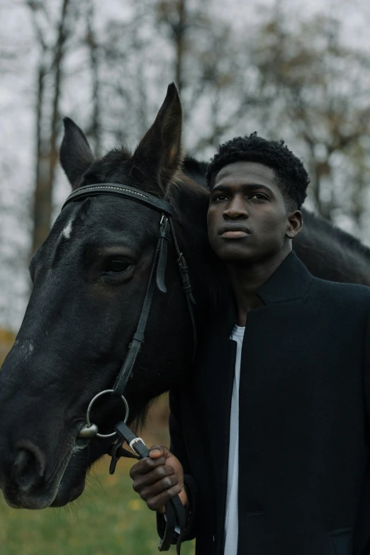 the man stands near the horse, he is holding it with his hand